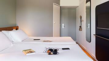 Quarto de hotel com duas camas, um espelho, uma televisão e uma porta que dá para outro espaço.