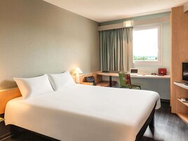 Habitación de hotel con una cama grande, un escritorio con una computadora portátil, una silla, un televisor y una ventana con cortinas.
