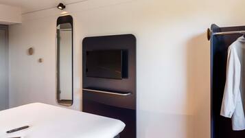 Una habitación de hotel moderna con una cama, un televisor montado en un panel negro, un espejo y un perchero.