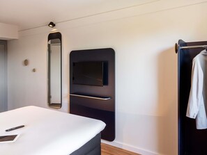 A modern hotel room with a bed, a TV mounted on a black panel, a mirror, and a towel rack.