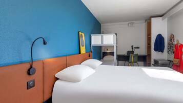 A hotel room with a bunk bed, a desk with a chair, a suitcase, and a coat rack with jackets.
