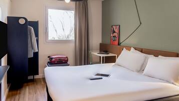 Habitación de hotel con cama, escritorio, silla, ventana con cortinas, una obra de arte en la pared y una lámpara colgante.