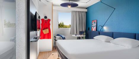 Una habitación de hotel moderna con una cama, un escritorio, una silla, un televisor, una ventana con cortinas y una pared de acento azul.