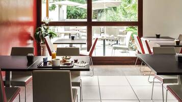 Un comedor con mesas y sillas, un amplio ventanal con vista a la terraza y una planta en maceta.