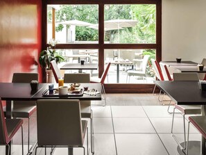 A dining area with tables and chairs, a large window with a view of outdoor seating, and a potted plant.
