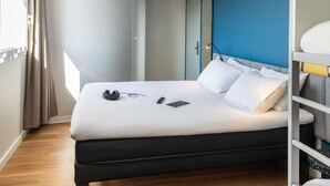 A hotel room with a bed, a bedside table, a lamp, and a window with curtains.