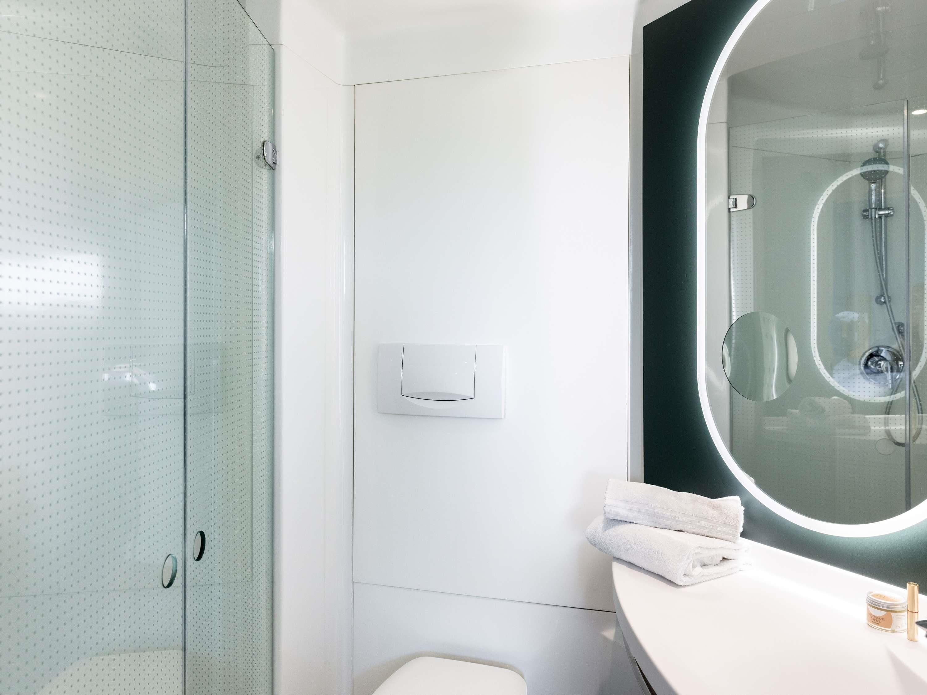 Een moderne badkamer met een douchecabine van glas, een witte wastafel met een ronde spiegel en een toilet.