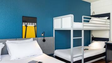 Habitación de hotel con una litera, una cama individual, una obra de arte en la pared, una lámpara de noche y un control remoto sobre la cama.