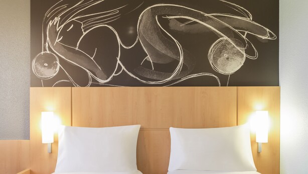 Habitación de hotel con dos camas, cabecero de madera y luces fijadas a la pared.