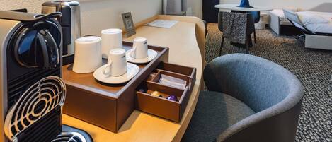 Ein Hotelzimmer mit einem Bett, einem Schreibtisch mit Kaffeemaschine, einem Sessel und einem kleinen Tisch mit einem Laptop.