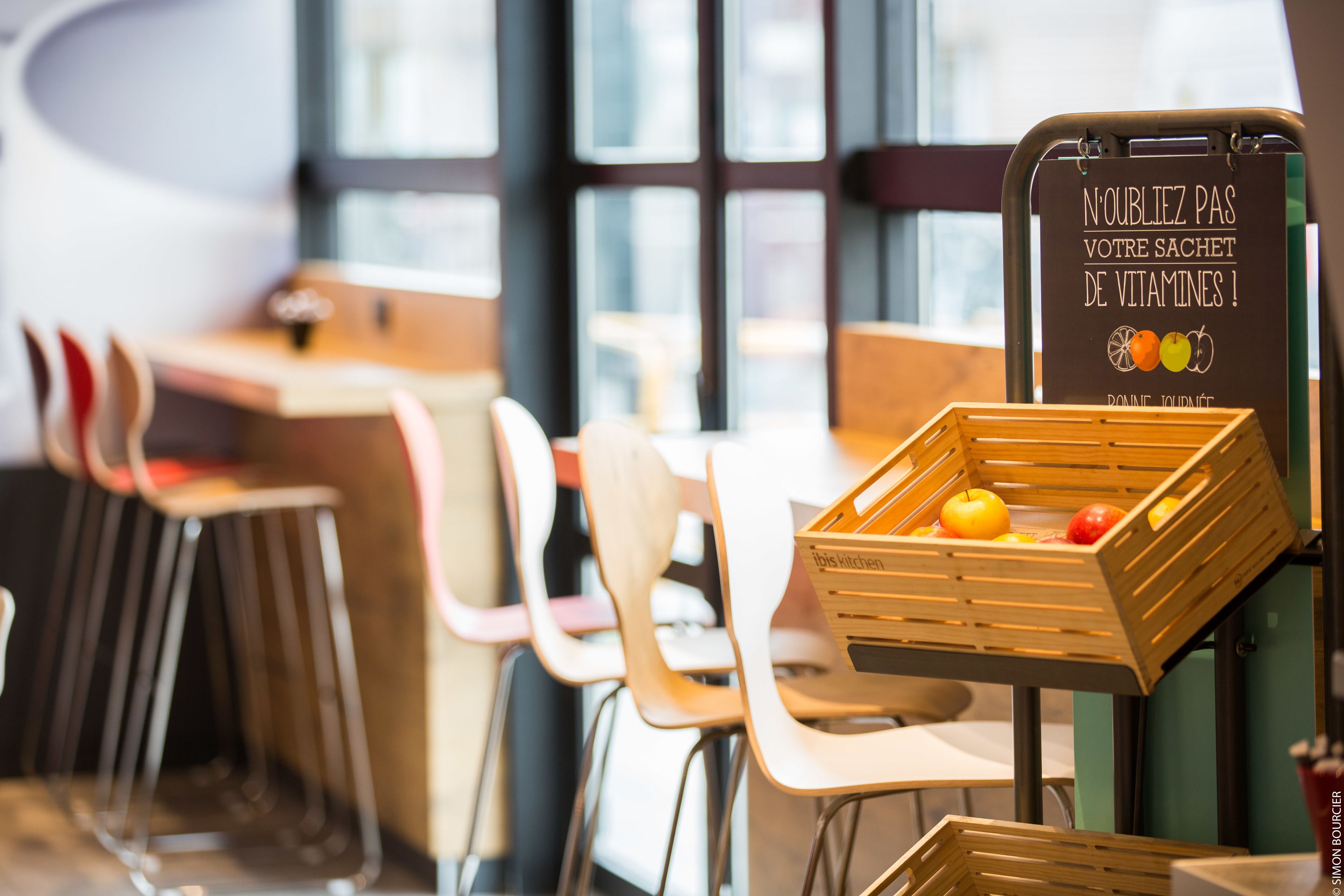 Interior de restaurante con mesas, sillas y una pizarra, adornado con cajas de madera llenas de frutas.