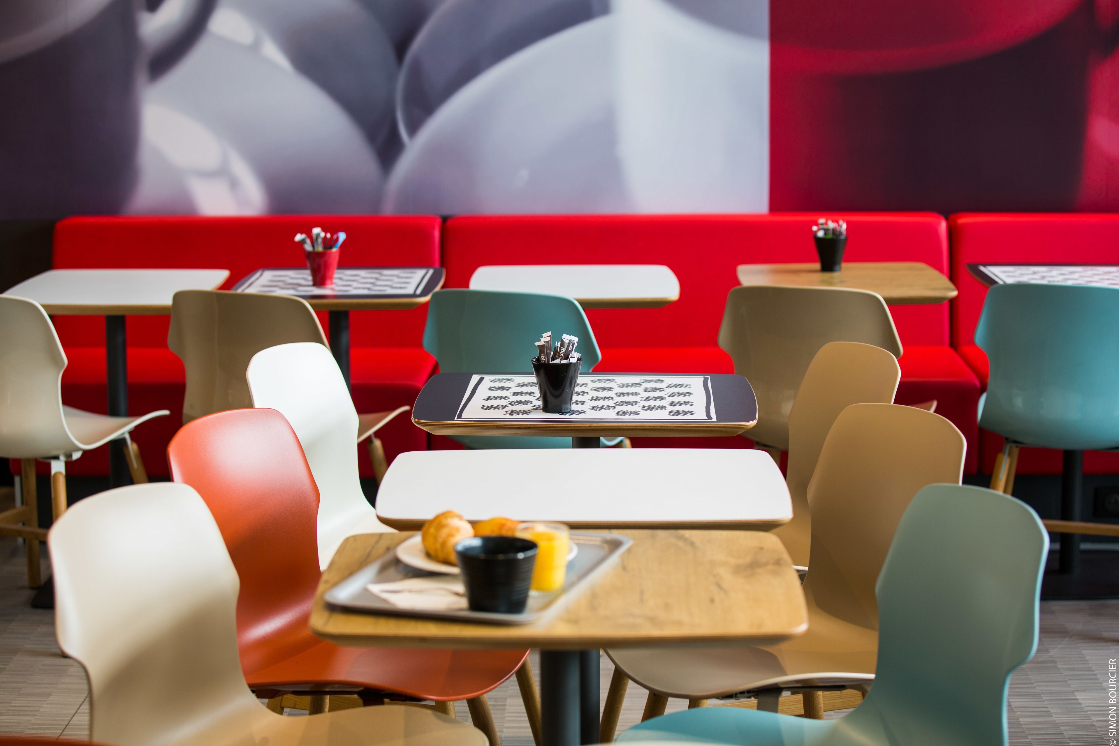 Un interior de restaurante moderno con asientos rojos, varias mesas y sillas.