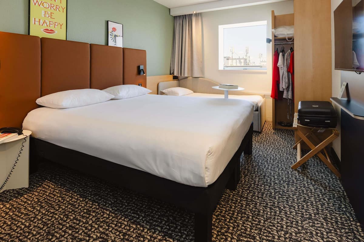 Quarto de hotel com uma cama grande, mesas de cabeceira, escrivaninha, guarda-roupa e janela com vista para a cidade.