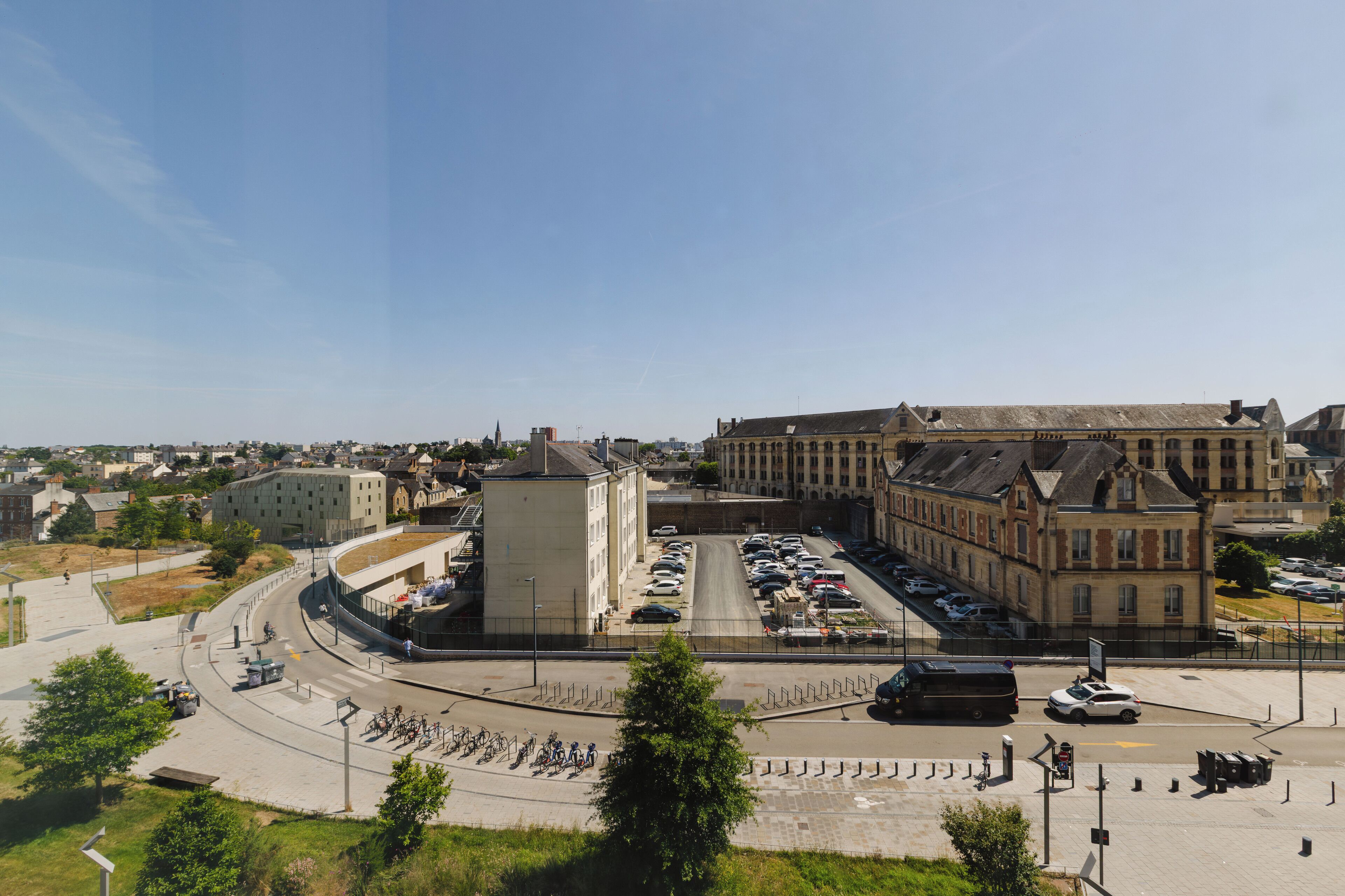 A large building with a central courtyard, surrounded by parked cars and a roundabout.
