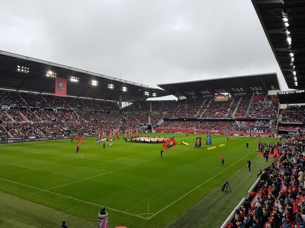 Um estádio grande com vários níveis de assentos, um campo central e algumas pessoas no campo.