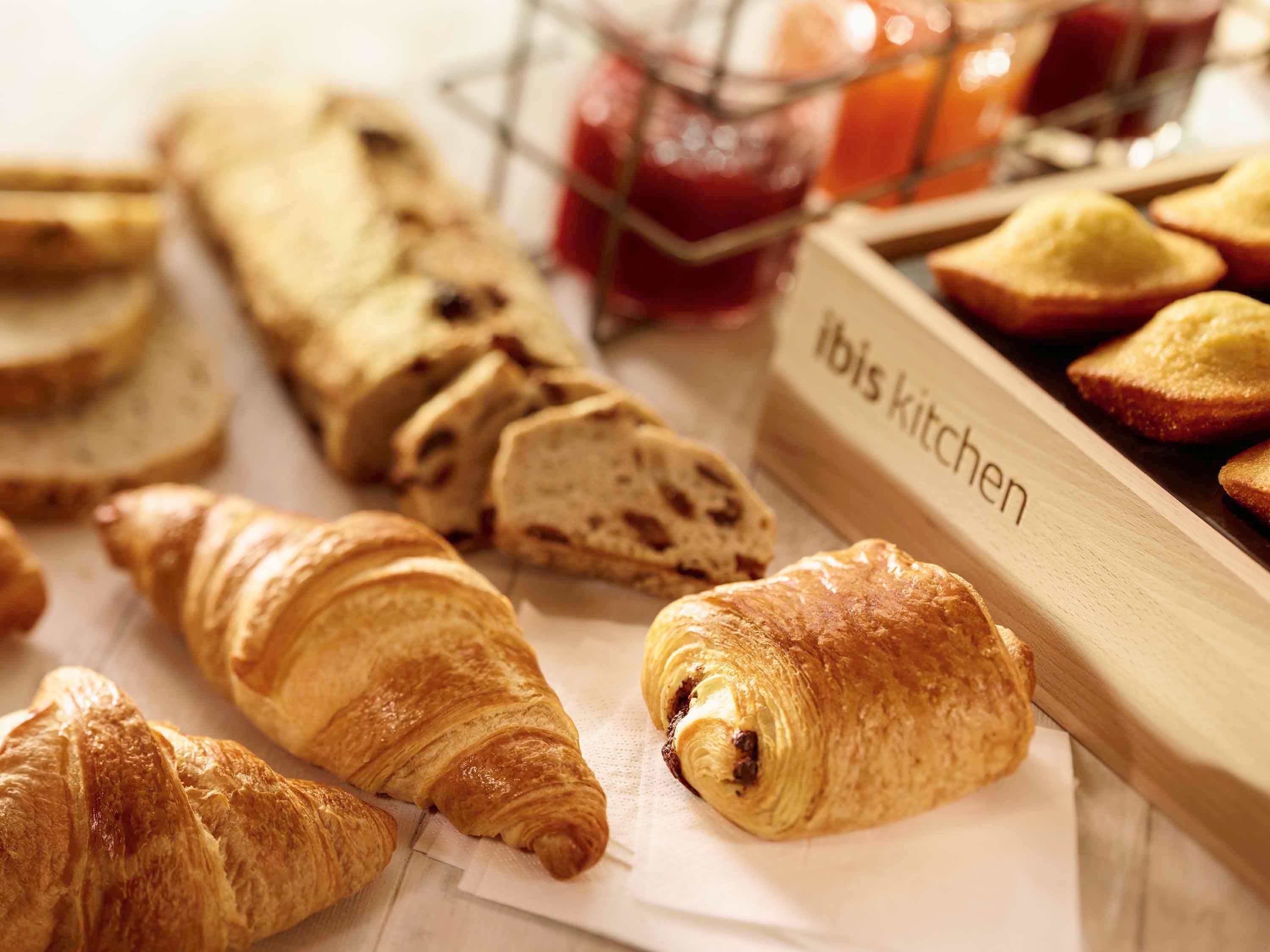 A variety of baked goods including croissants and bread, arranged on a table with a label reading "Ibis Kitchen".