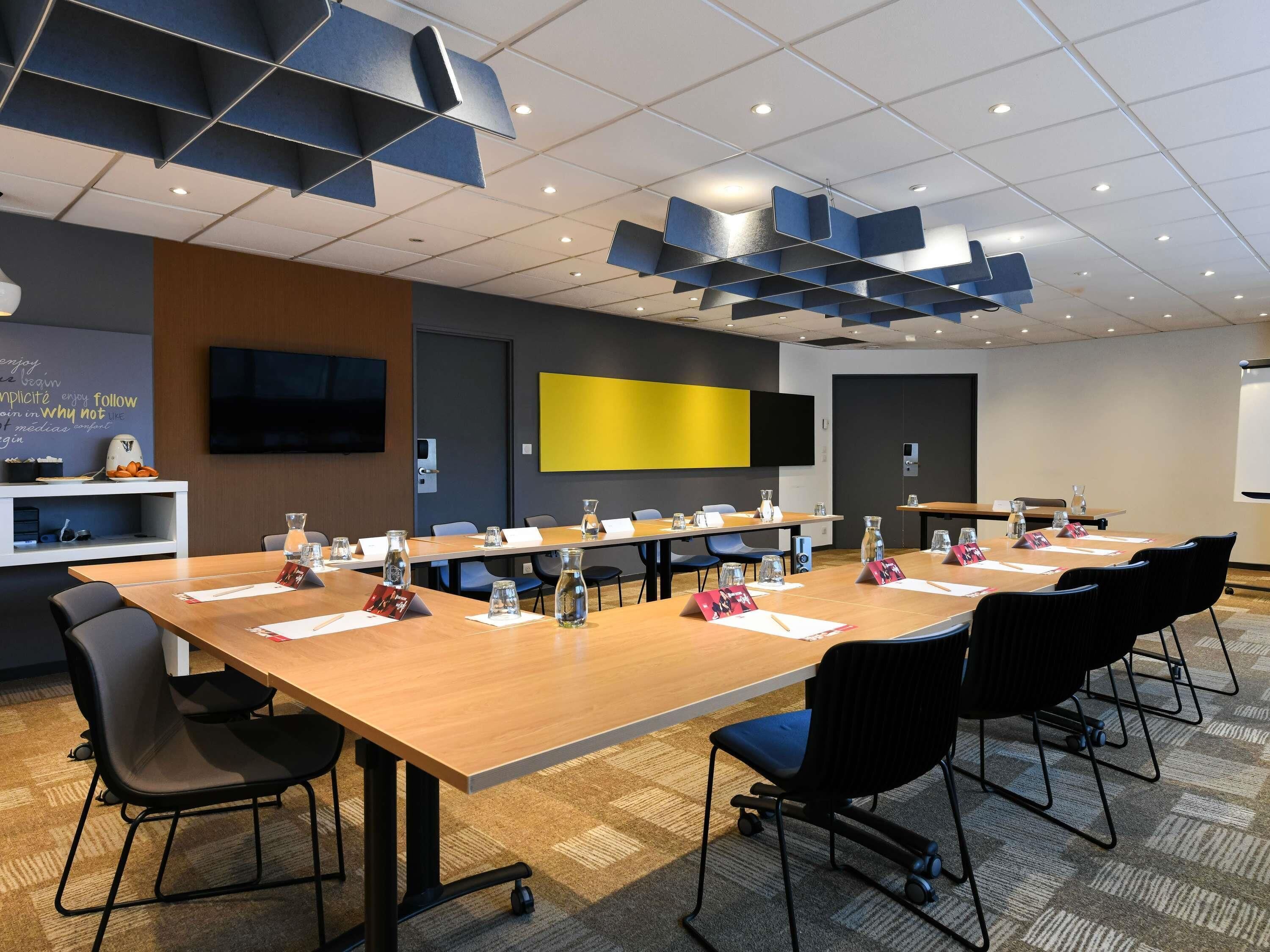 Un salón de conferencias con una mesa larga, sillas, una televisión y una pantalla amarilla.