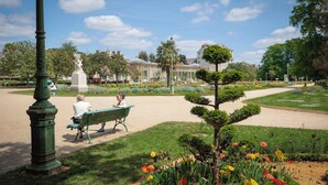Un parque con una estatua, bancos y un jardín de flores bien cuidado.