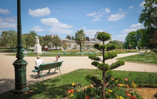 Un parc agrémenté d’une statue, de bancs et d’un jardin fleuri bien entretenu.