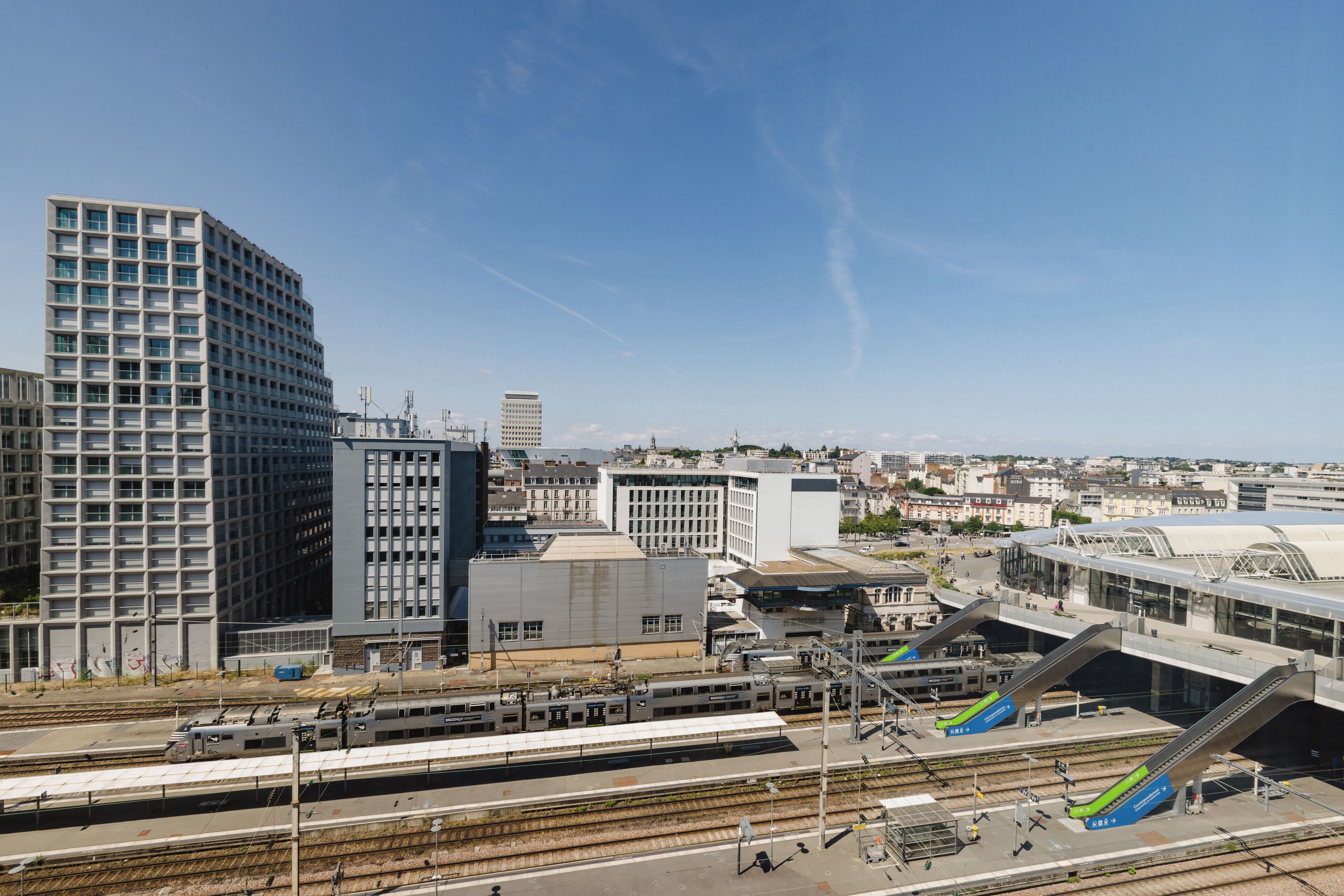 A modern urban train station with multiple platforms and tracks, surrounded by high-rise buildings.