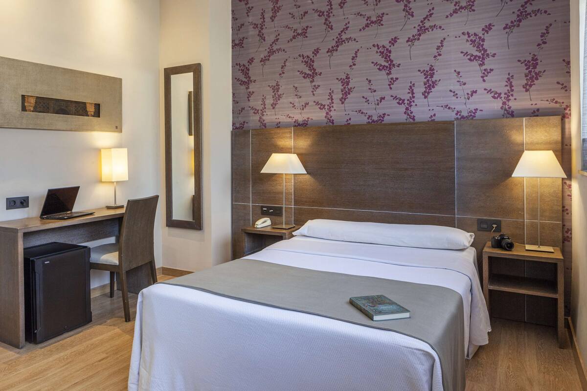 Una habitación de hotel con cama, escritorio, silla y un pequeño refrigerador.