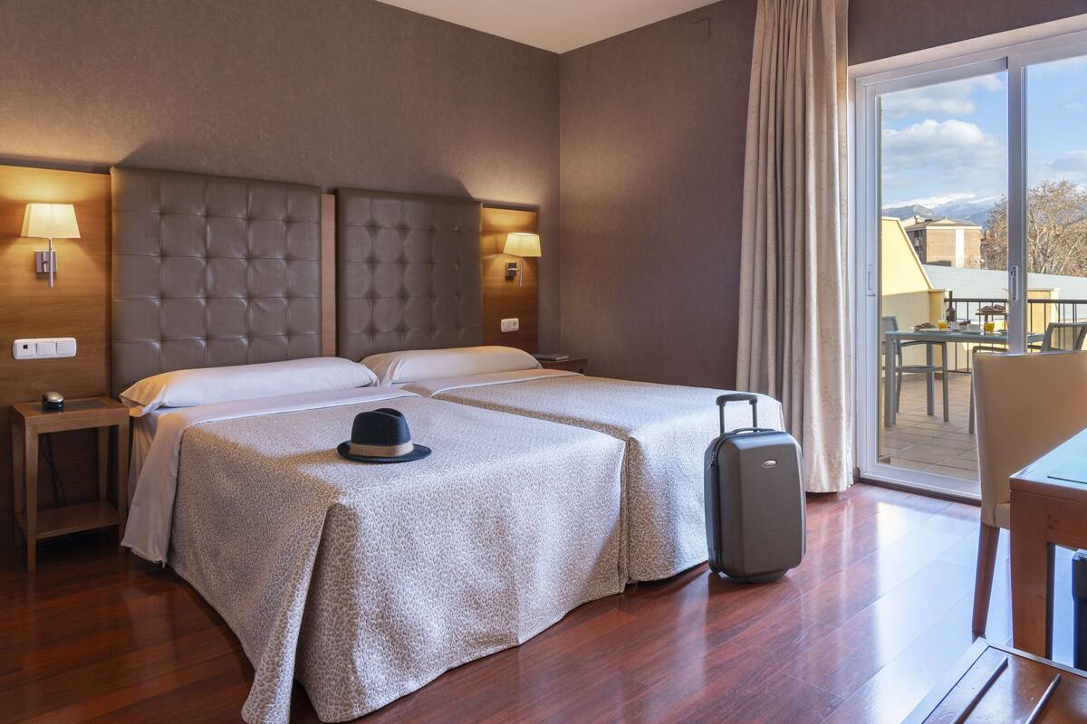 Una habitación de hotel con dos camas, una maleta y un comedor con mesa y sillas.