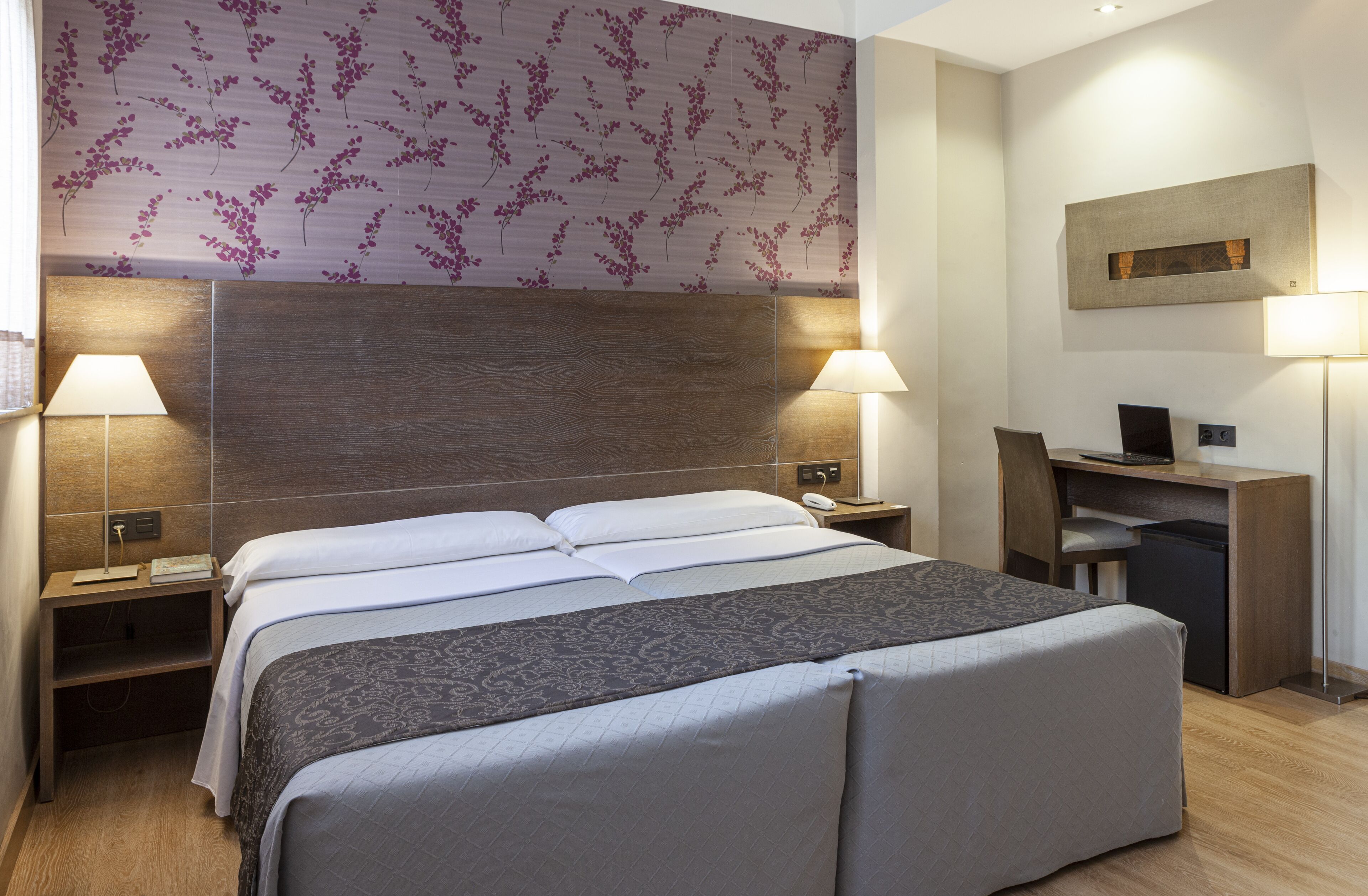 Habitación de hotel con una cama grande, dos mesitas de noche con lámparas, un escritorio con silla y un refrigerador pequeño.