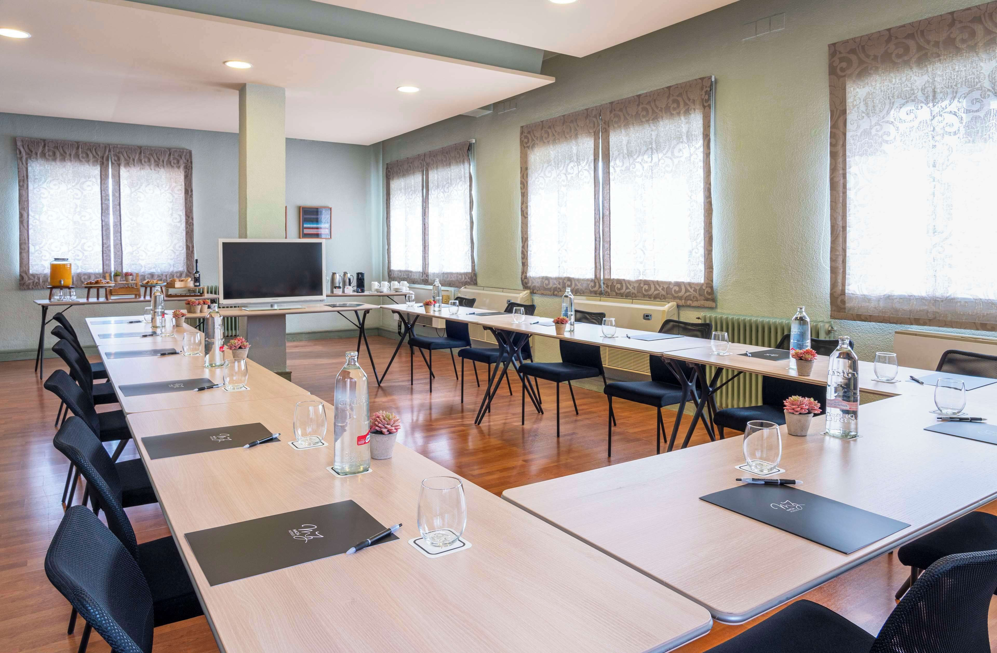 A conference room with long tables, chairs, a large screen, and windows with curtains.