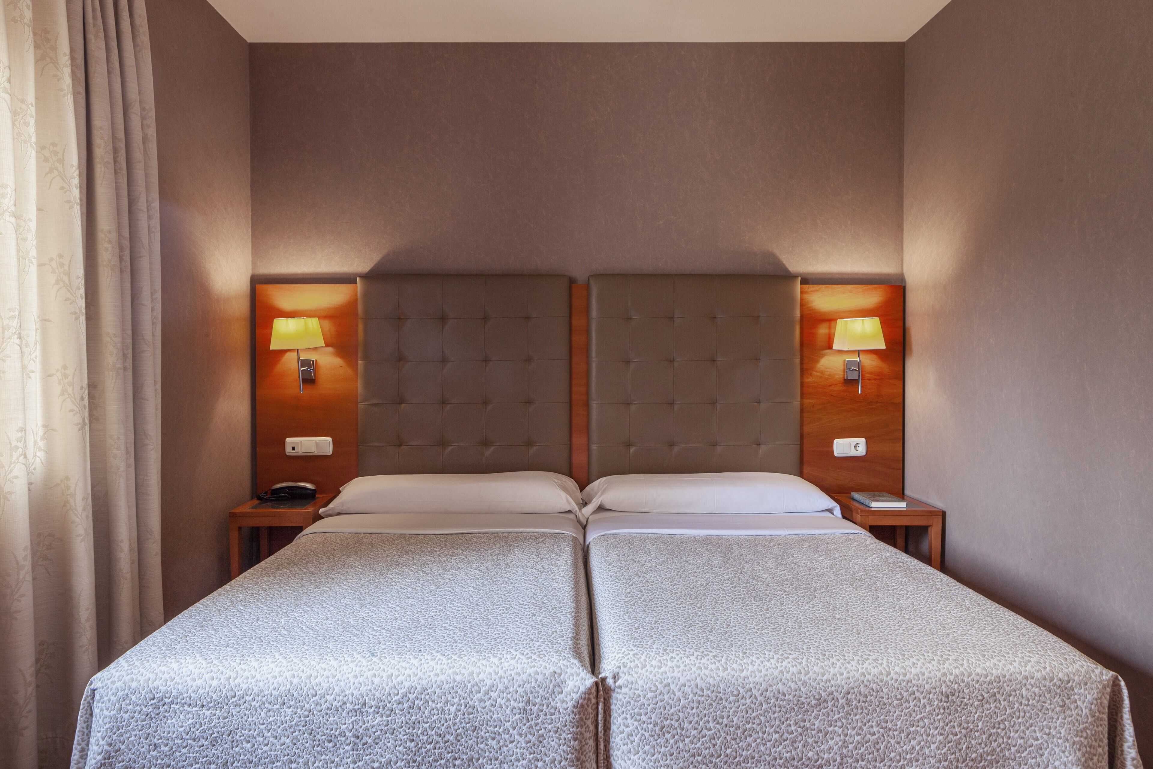 A double bed with a tufted headboard, two bedside tables with lamps, and a curtain on the left.