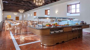 A spacious dining area with a central buffet counter, wooden chairs, and a high ceiling with exposed beams.