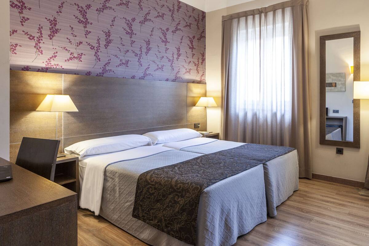 Habitación de hotel con una cama grande, dos mesitas de noche con lámparas, un escritorio y un espejo.