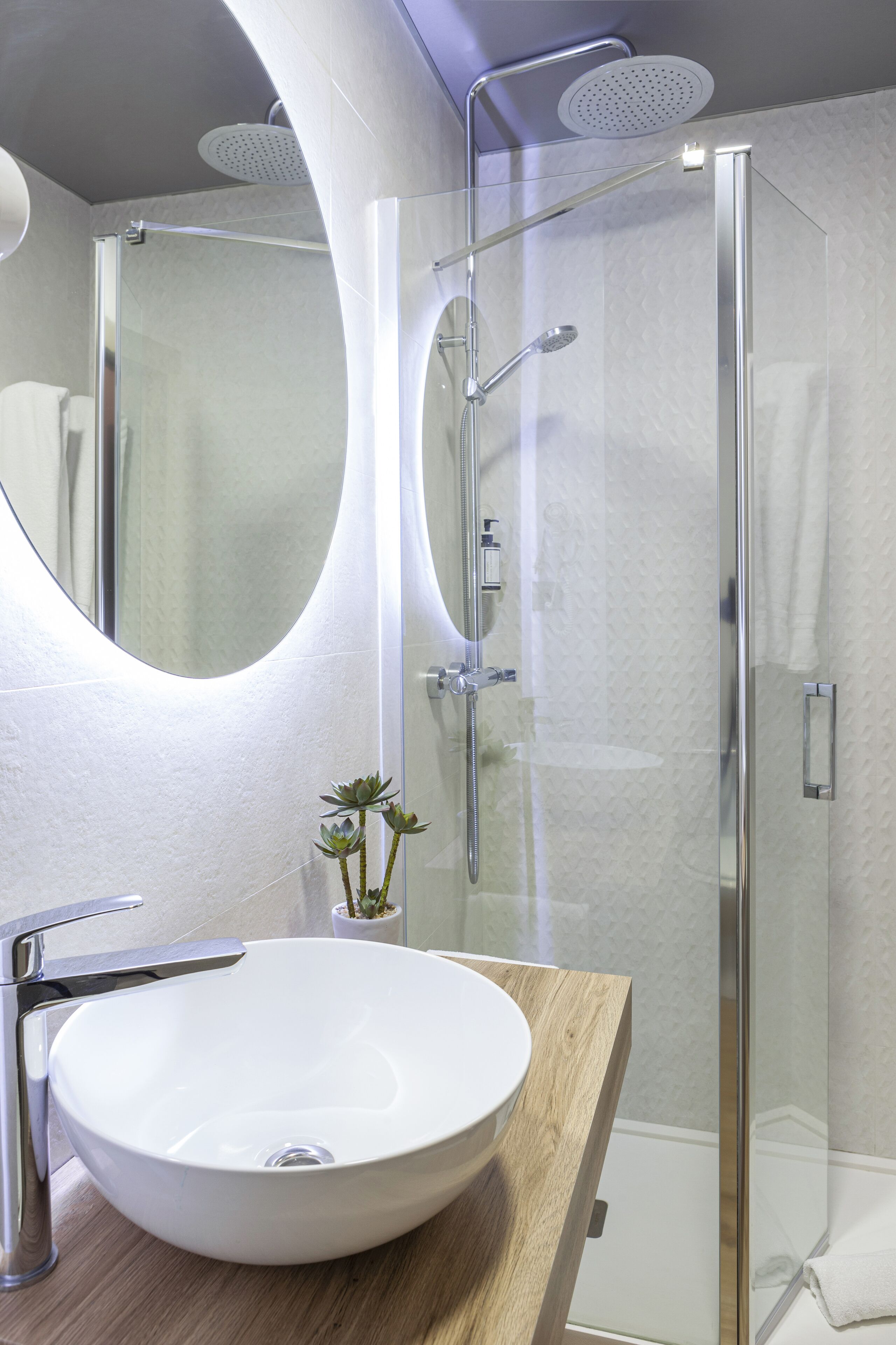 Un baño moderno con cabina de ducha de vidrio, un espejo redondo y una encimera de madera con lavamanos blanco.