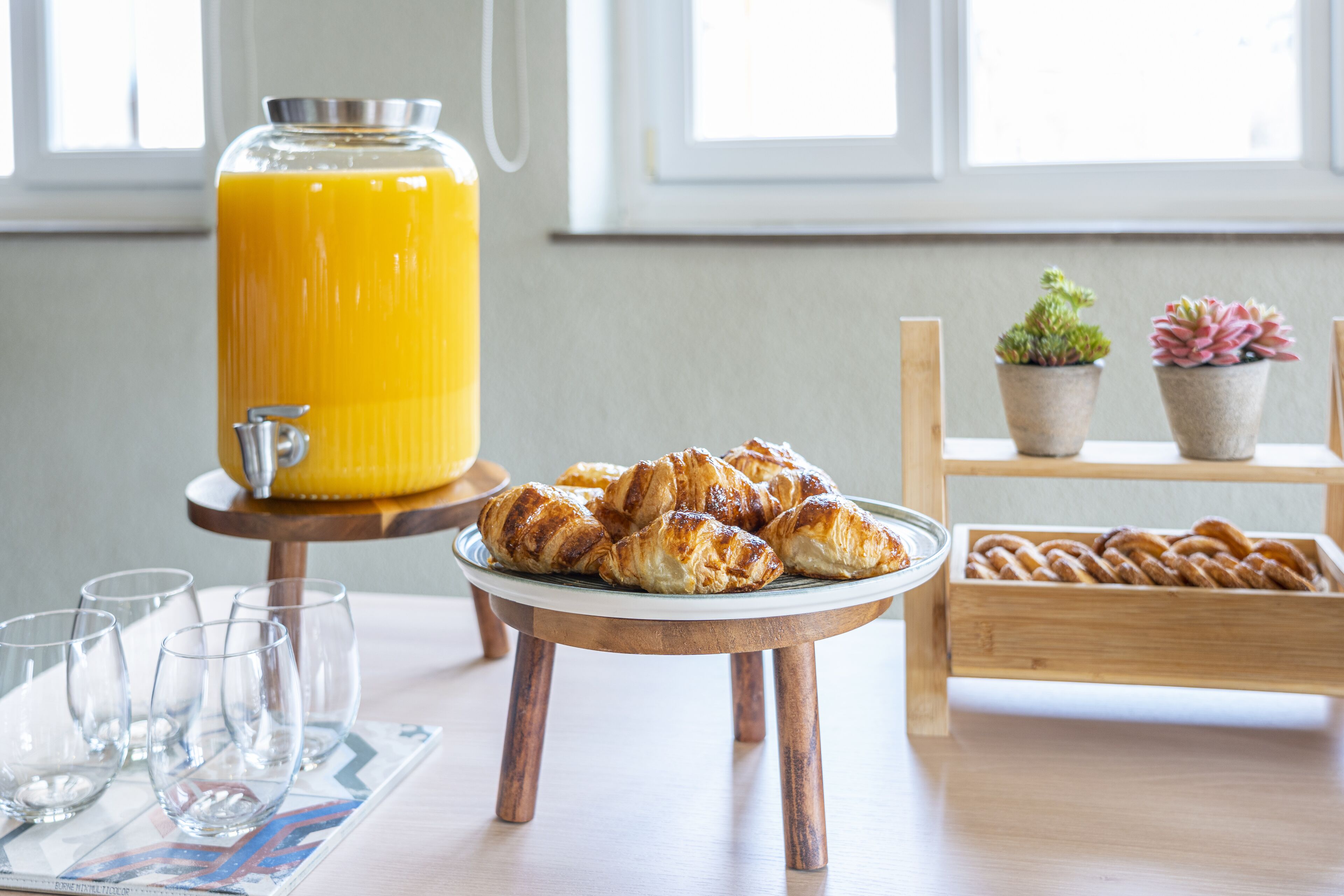 Un desayuno con croissants, un vaso de zumo de naranja y una bandeja de pasteles.