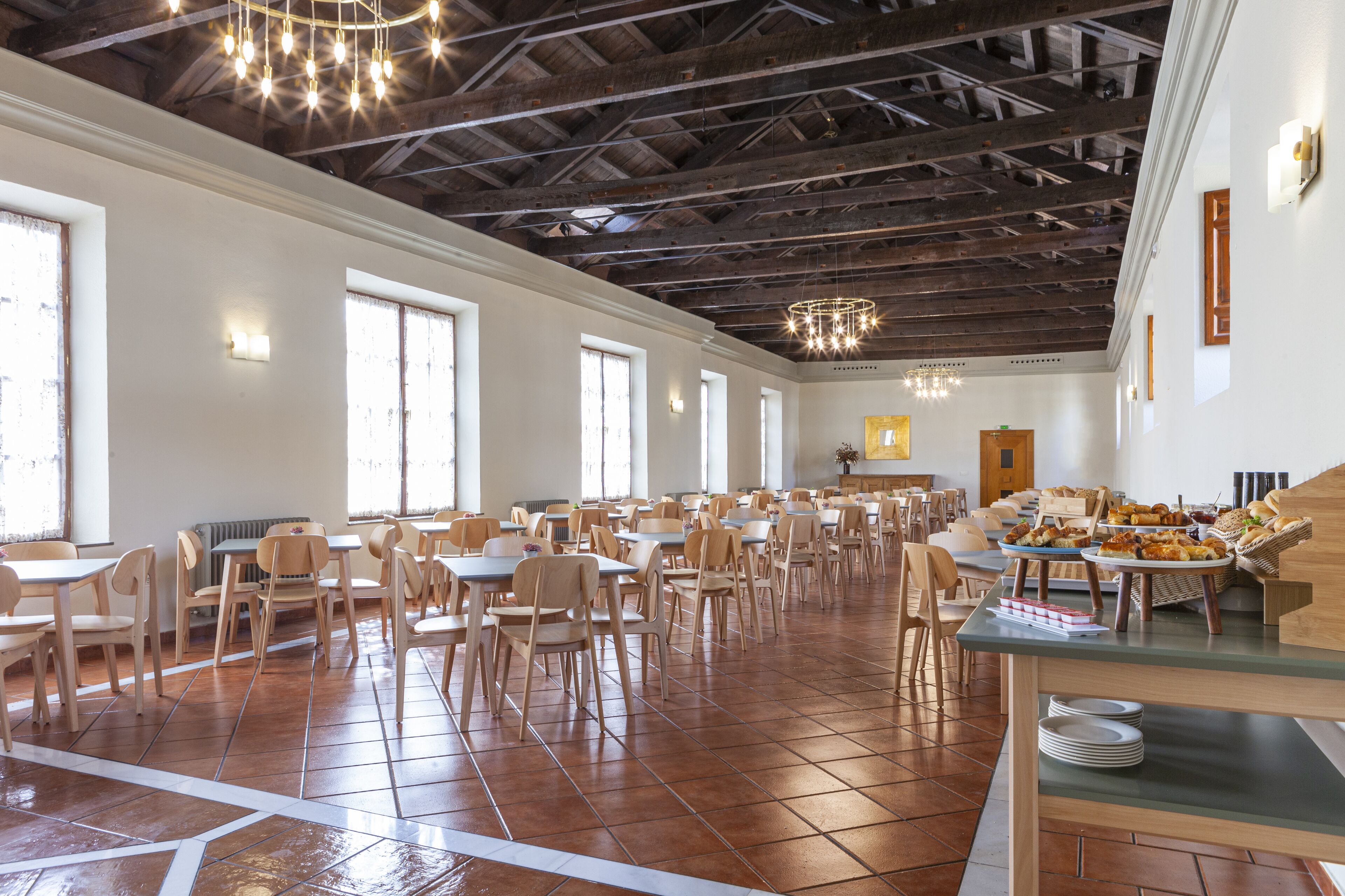 Ruime eetruimte met tal van tafels en stoelen, een hoge plafond met zichtbare balken, en een buffetopstelling aan de rechterkant.