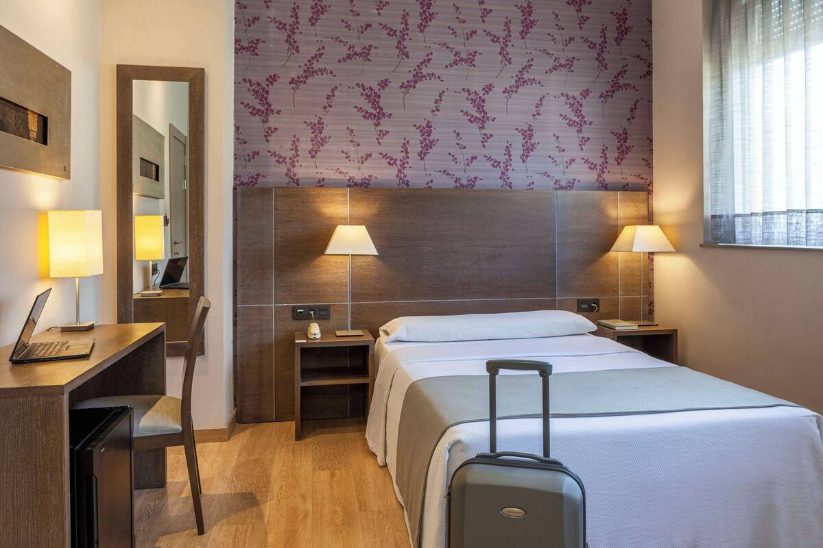 Habitación de hotel con cama, escritorio, silla y una maleta.