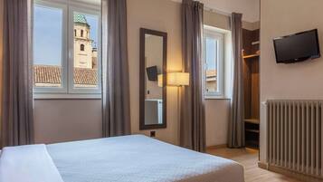 A hotel room with a bed, a mirror, a TV, a window with curtains, and a radiator.