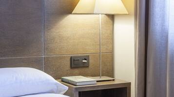 Une chambre d’hôtel avec un lit, une table de chevet avec une lampe, un livre et un mur orné d’un motif floral.