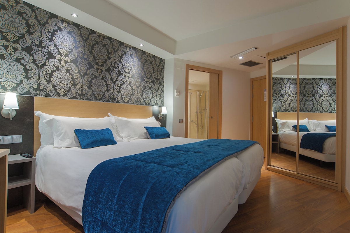 Una habitación de hotel moderna con una cama grande, una mesita de noche, un espejo y un armario.