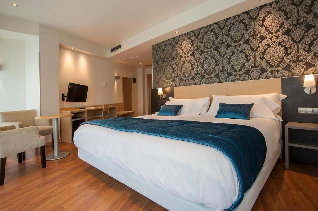 A hotel room with a large bed, a desk, a chair, and a television.