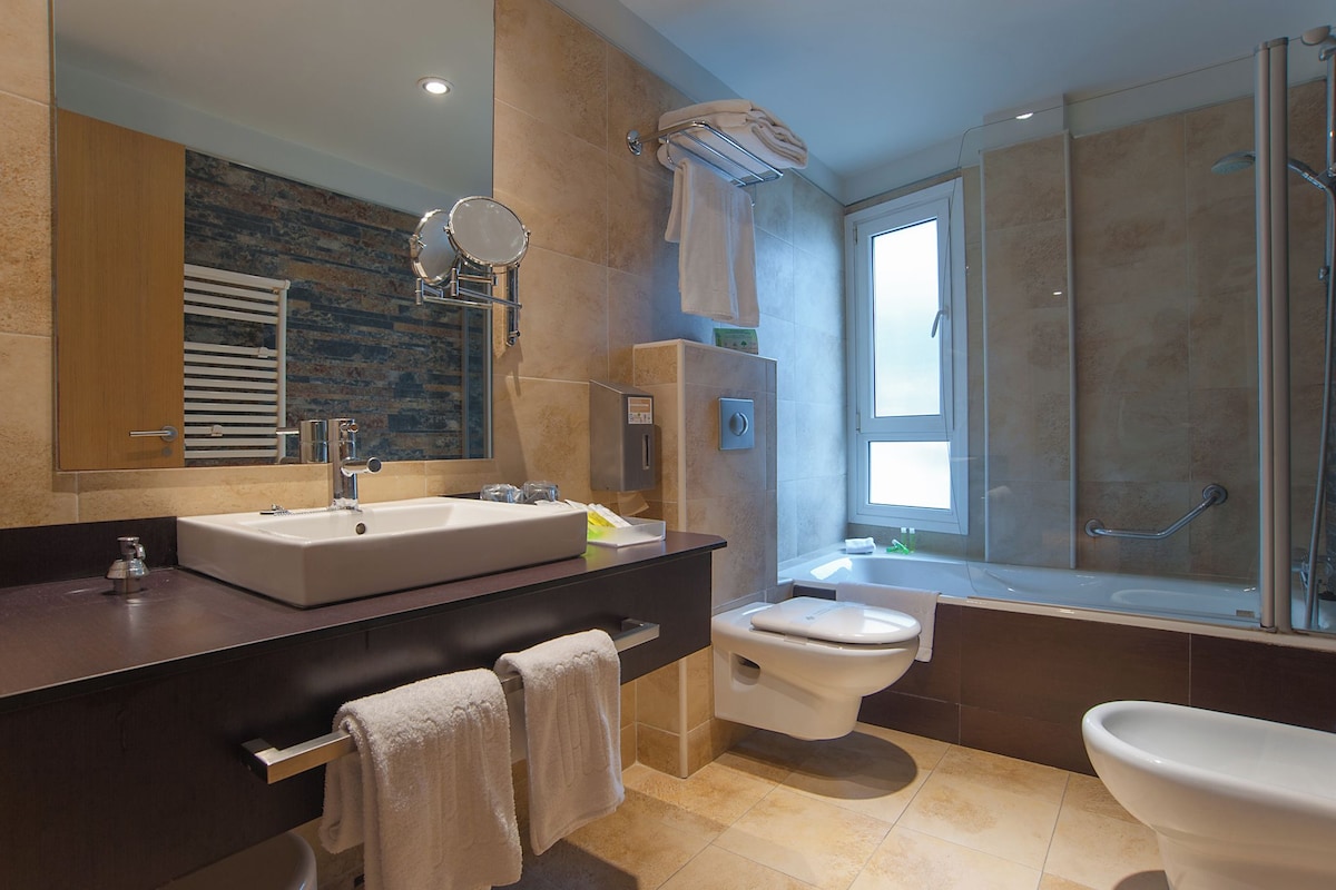 Un baño moderno con un espejo grande, dos lavamanos, un inodoro y una zona de ducha.