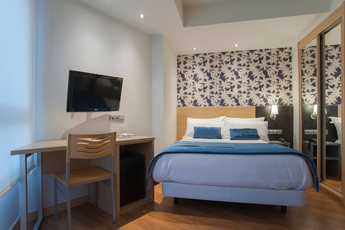 Un dormitorio con cama, un escritorio con silla, televisor y pared con diseño.