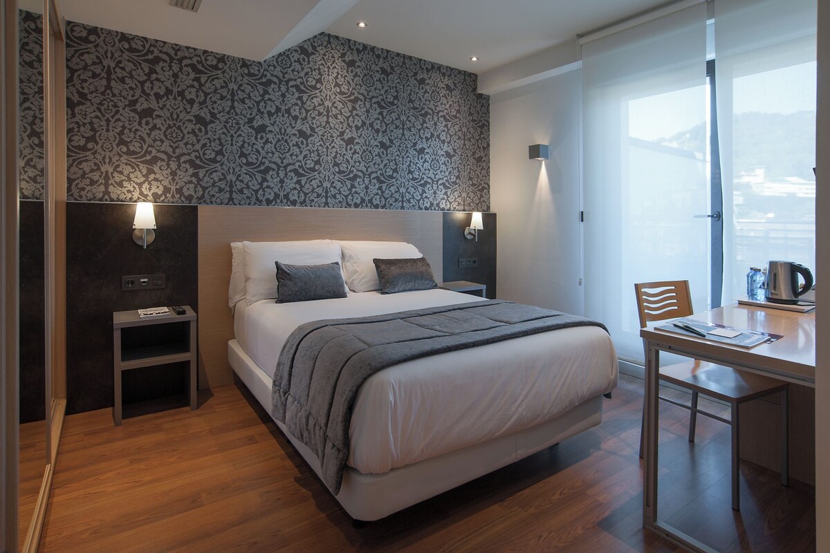 Una habitación de hotel moderna con una cama grande, mesitas de noche, un escritorio y una silla.