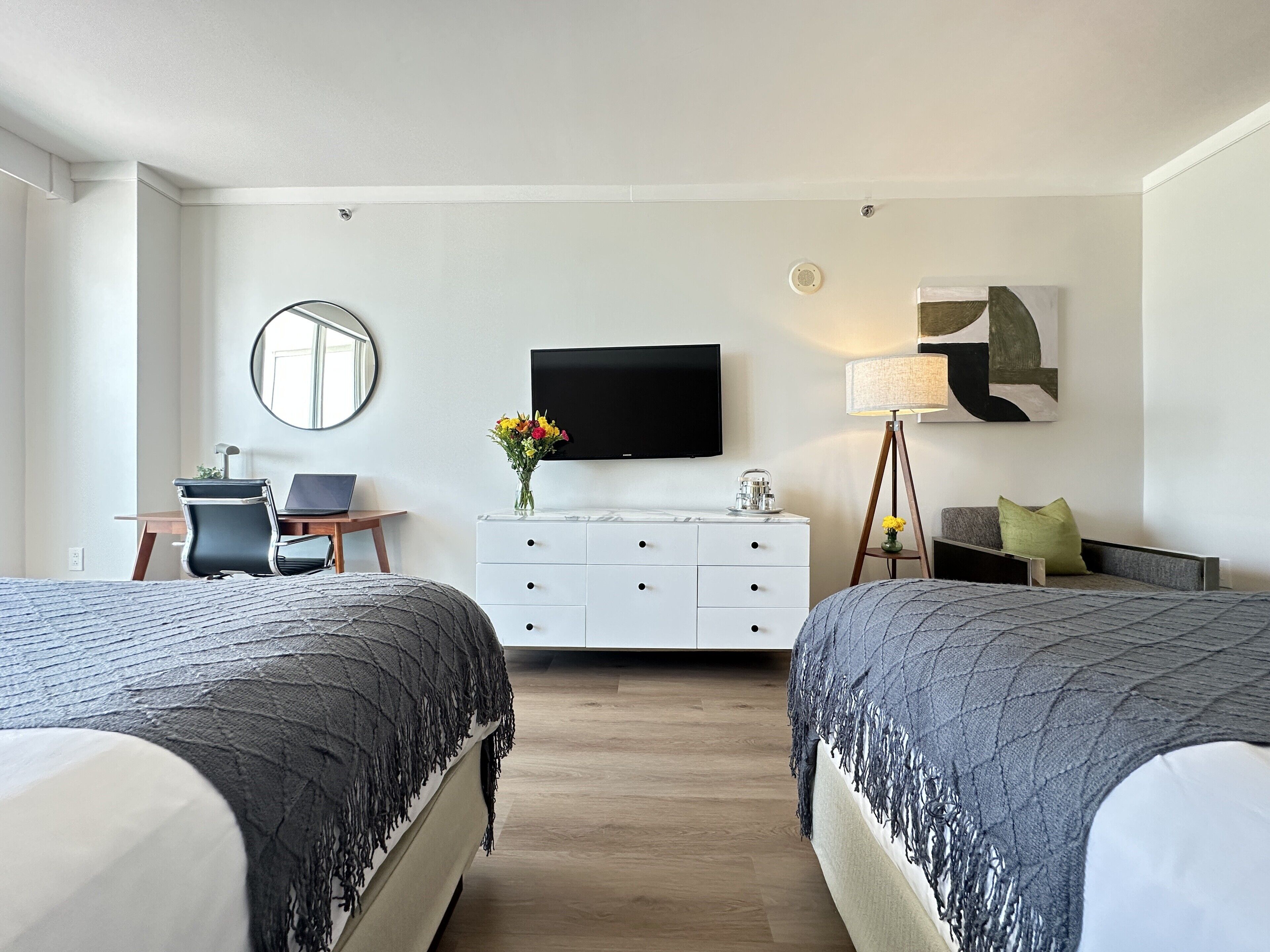 Una habitación de hotel moderna con dos camas, un escritorio, un televisor y una mesita de noche con lámpara.