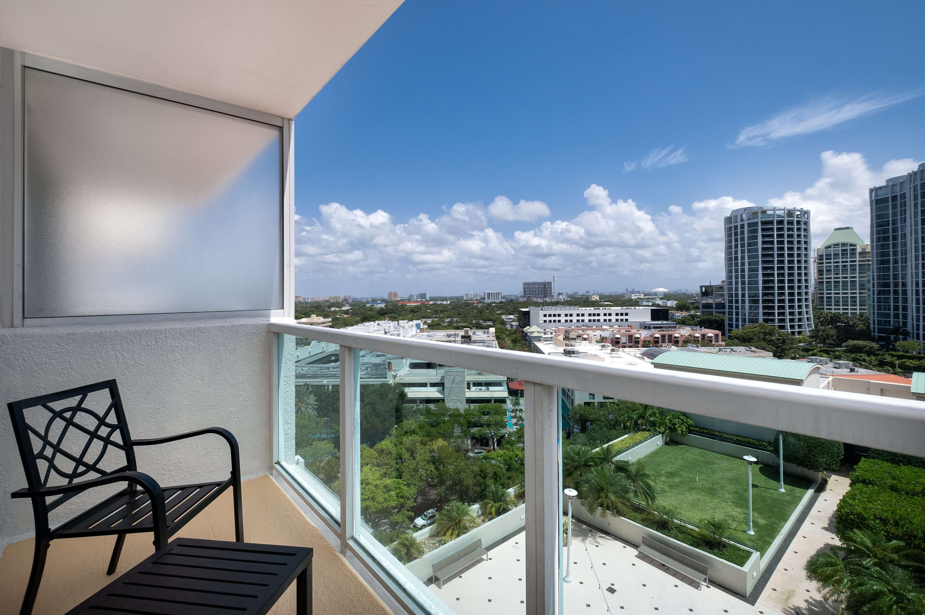 A balcony with a view of a cityscape, a chair, and a table.