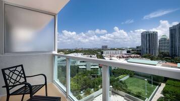 A balcony with a view of a cityscape, a chair, and a table.