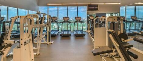 A gym with treadmills, weight machines, and a large window offering a city view.