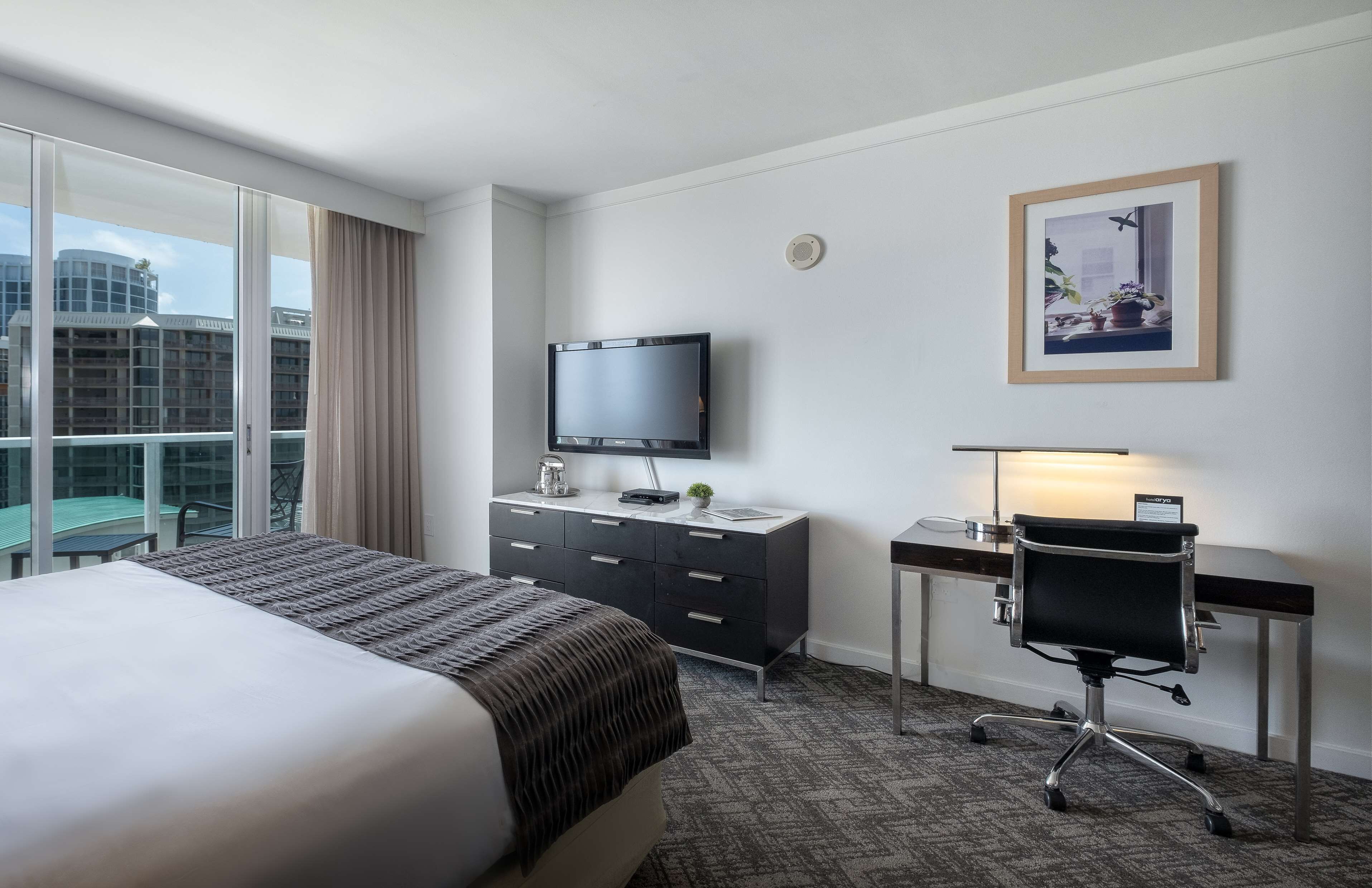 Hotelkamer met een groot bed, een bureau met stoel, een televisie en een raam met uitzicht op gebouwen.
