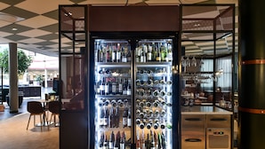 A modern interior with a wine refrigerator stocked with various bottles and glasses, a wooden desk with drawers, and a large potted plant. - Scandic Star (Lund)