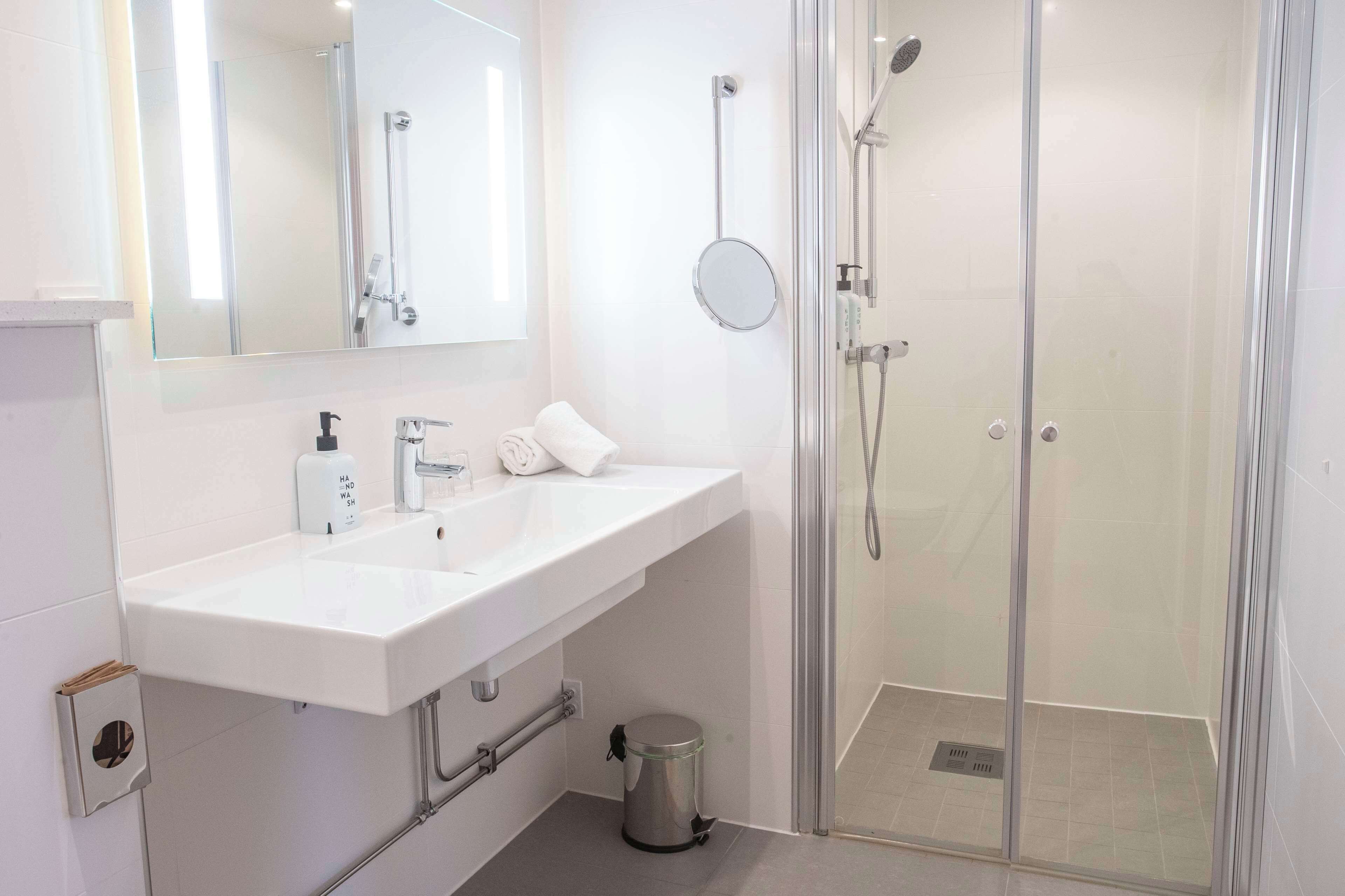Un baño moderno con lavamanos blanco, espejo y ducha con mampara de vidrio.