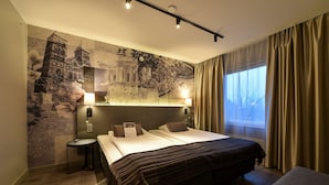 A hotel room with a large bed, a nightstand, a wall mural, a window with curtains, and a lamp. - Scandic Star (Lund)